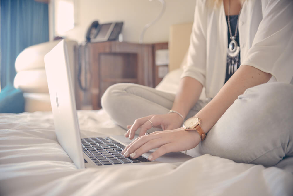 A woman sitting on a bed in a hotel room using her laptop